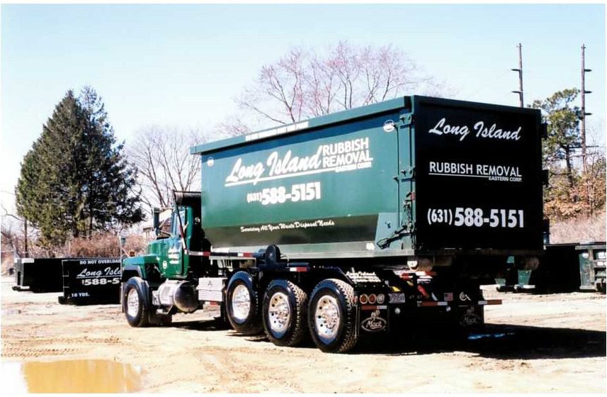A green dumpster truck from Long Island Rubbish Removal parked in a yard, displaying the company name and contact information.