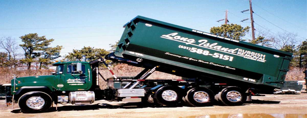 Green dump truck with 'Long Island Rubbish Removal' branding, lifting a large container in an outdoor setting.